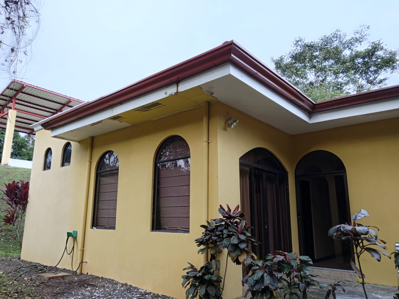 Casa amarilla con canoas color vino y ventanas arqueadas